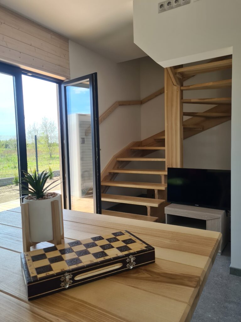 Stół z rośliną i zestawem szachowym w drewnianym domku, z widokiem na ogród i schody.