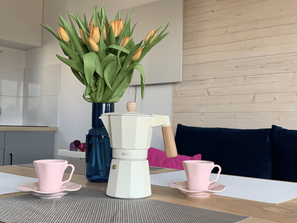 Wazon z tulipanami, kawiarka i filiżanki na stole w nowoczesnym domku letniskowym.